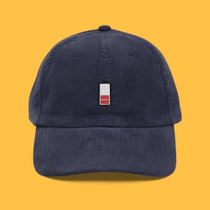 Könnte beinhalten: Marineblaue Cord-Baseballkappe mit gesticktem Akku-Symbol. Die Kappe hat einen gebogenen Schirm und einen verstellbaren Riemen. Das Batterie-Symbol ist weiß und rot.