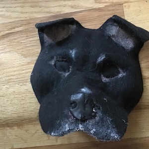 May include: Black felt dog mask with a black felt nose and ears. The mask is unfinished and has some white fuzz on the edges.