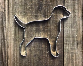 May include: A metal cookie cutter in the shape of a dog. The cutter is silver and has a smooth finish.