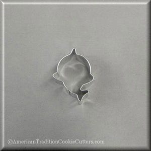 May include: A silver metal cookie cutter shaped like a dolphin. The cutter is on a grey background.