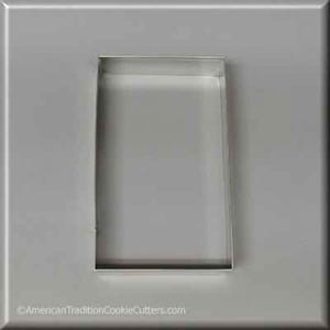 May include: A silver metal cookie cutter in the shape of a rectangle. The cookie cutter is on a gray background.