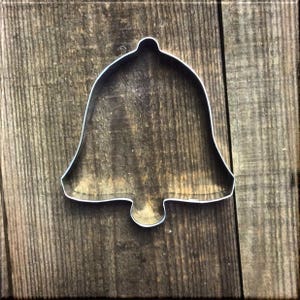 May include: A silver metal bell cookie cutter on a wooden background.
