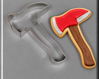 May include: A silver metal axe-shaped cookie cutter next to a decorated axe-shaped biscuit. The biscuit features a bright red blade with silver edges and a brown wood-grain textured handle, all outlined in a light tan biscuit dough border.