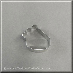 May include: A silver-colored metal cookie cutter in the shape of a foot. The cutter has a simple, clean design with a rounded heel and toes. The cutter is on a gray surface.