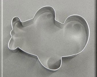 May include: A silver metal cookie cutter shaped like a cartoon airplane. The cutter is on a gray background.