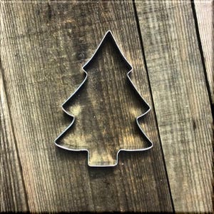May include: A metal cookie cutter shaped like a Christmas tree. The cutter is on a rustic wooden background.
