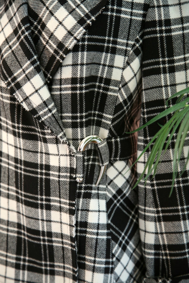 Peut inclure: Gros plan sur une veste &agrave; carreaux noirs et blancs avec un fermoir argent&eacute;. La veste pr&eacute;sente un motif &agrave; carreaux classique en noir et blanc, avec une fermeture &agrave; fermoir argent&eacute;. Le tissu semble &ecirc;tre une mati&egrave;re tiss&eacute;e.