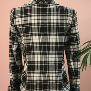 Peut inclure: Blazer &agrave; carreaux noirs et blancs pr&eacute;sent&eacute; sur un mannequin. La veste pr&eacute;sente un motif tartan classique, un col crant&eacute; et des manches longues. Le tissu semble &ecirc;tre de poids moyen, adapt&eacute; aux temp&eacute;ratures plus fra&icirc;ches. V&ecirc;tement polyvalent.