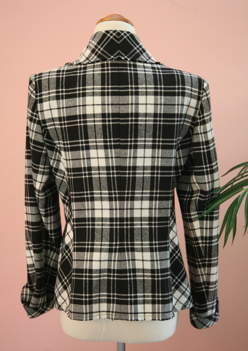 Peut inclure: Blazer &agrave; carreaux noirs et blancs pr&eacute;sent&eacute; sur un mannequin. La veste pr&eacute;sente un motif tartan classique, un col crant&eacute; et des manches longues. Le tissu semble &ecirc;tre de poids moyen, adapt&eacute; aux temp&eacute;ratures plus fra&icirc;ches. V&ecirc;tement polyvalent.