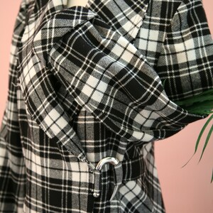 Peut inclure: Un manteau &agrave; carreaux noir et blanc avec un col crant&eacute; et une ceinture &agrave; boucle argent&eacute;e. Le manteau pr&eacute;sente un motif tartan classique et une silhouette ajust&eacute;e. Le tissu semble &ecirc;tre une mati&egrave;re tiss&eacute;e, adapt&eacute;e aux temps plus frais.
