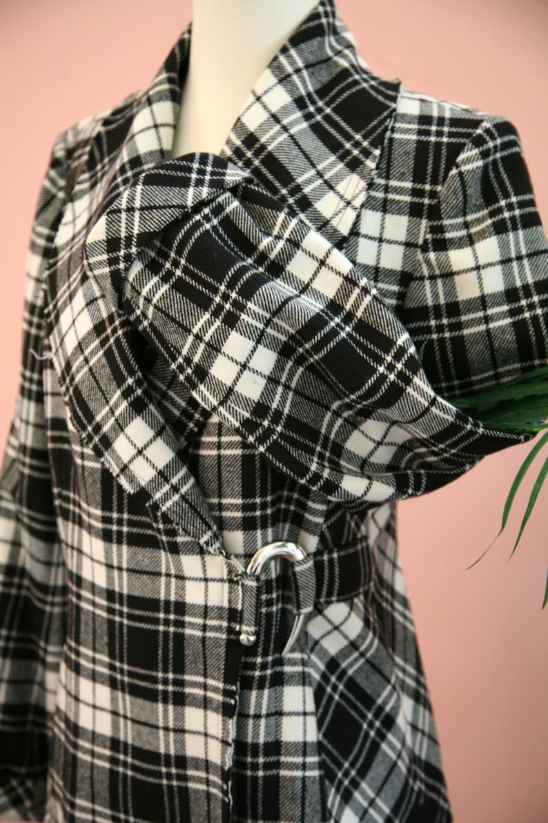 Peut inclure: Un manteau &agrave; carreaux noir et blanc avec un col crant&eacute; et une ceinture &agrave; boucle argent&eacute;e. Le manteau pr&eacute;sente un motif tartan classique et une silhouette ajust&eacute;e. Le tissu semble &ecirc;tre une mati&egrave;re tiss&eacute;e, adapt&eacute;e aux temps plus frais.