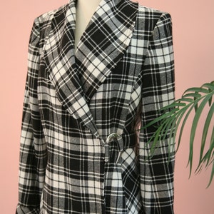 Peut inclure: Un blazer &agrave; carreaux noirs et blancs avec un col ch&acirc;le et une fermeture &agrave; boucle argent&eacute;e. Le blazer est pr&eacute;sent&eacute; sur un mannequin et a des manches retrouss&eacute;es. Le tissu pr&eacute;sente un motif tiss&eacute; classique.