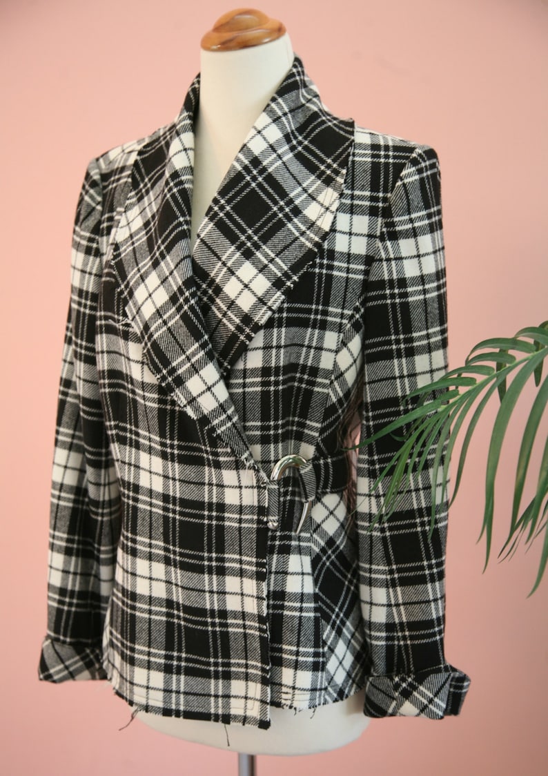 Peut inclure: Un blazer &agrave; carreaux noirs et blancs avec un col ch&acirc;le et une fermeture &agrave; boucle argent&eacute;e. Le blazer est pr&eacute;sent&eacute; sur un mannequin et a des manches retrouss&eacute;es. Le tissu pr&eacute;sente un motif tiss&eacute; classique.