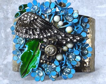 Vintage enamel pin bracet with blue petals, green leaves, an angle wing and cross.