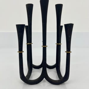 以下が含まれることがあります： 6本の燭台が付いた黒い金属製の燭台。燭台は湾曲しており、上部に金色のアクセントがあります。