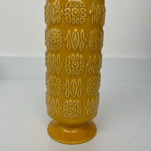 Peut inclure: Un vase en céramique jaune avec un motif géométrique. Le vase a une base large et un corps cylindrique.