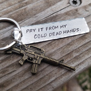 May include: A silver keychain with a small metal gun charm and a tag that reads "Pry it from my cold dead hands."