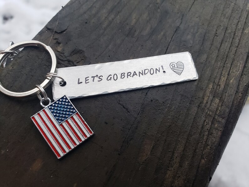 May include: A silver keychain with a small American flag charm and a metal tag that reads "LET'S GO BRANDON!" with a small American flag heart.