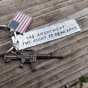 May include: A silver keychain with a small American flag charm, a miniature rifle charm, and a silver tag that reads "2nd Amendment The Right To Bear Arms".