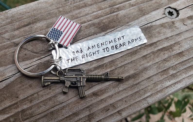 May include: A silver keychain with a small American flag charm, a miniature rifle charm, and a silver tag that reads "2nd Amendment The Right To Bear Arms".