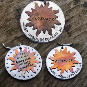 May include: A silver metal keychain with a copper sun design. The sun has the words "GODSMACK" and "NEVER MISUNDERSTAND ME" engraved on it. The other side of the keychain has the words "you are my SUNSHINE my only sunshine" engraved on it.