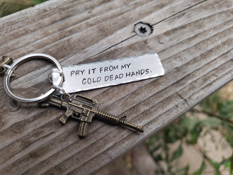 May include: A silver keychain with a small metal gun charm and a tag that reads "Pry it from my cold dead hands."