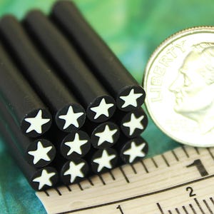 May include: A stack of twelve black cylindrical rods with white star-shaped centers, positioned next to a silver US dime and a white measuring tape showing a diameter of approximately 0.7 inches for each individual rod.