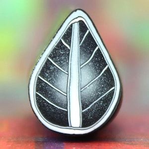 Op de afbeelding: Een zwart-witte blaadjesvormige hanger met een witte ader die door het midden loopt. De hanger heeft een getextureerd oppervlak.