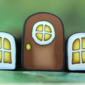 May include: A whimsical miniature house design featuring a brown door with a yellow window and a yellow doorknob, flanked by two arched windows with yellow panes. The windows and door have a white border.