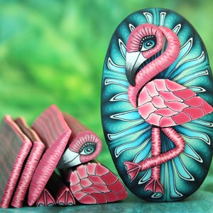May include: A pink flamingo with blue eyes and a teal background. The flamingo is made of polymer clay and has a detailed, textured surface.