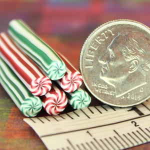 May include: Close-up of several miniature candy canes with red, white, and green stripes. A US dime coin and a ruler are next to the candy canes. The candy canes have a spiral design on the ends.