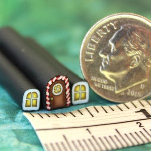 May include: Miniature polymer clay house with a brown door, red and white striped trim, and yellow windows. A U.S. dime coin and a ruler are next to the house. The house is made of black clay.