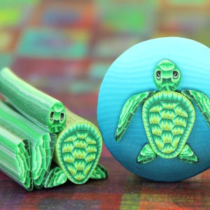 Peut inclure: Une figurine de tortue en pâte polymère verte et bleue avec un motif de carapace détaillé. La tortue est assise sur un fond bleu et vert.