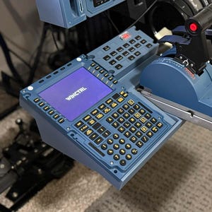 Könnte beinhalten: Ein blaues Flugsimulator-Bedienfeld mit zahlreichen Knöpfen, Schaltern und Hebeln. Das Panel enthält einen Bildschirm mit der Aufschrift "WINCTRL" und eine Tastatur. Das Design erinnert an ein Flugzeugcockpit und betont Realismus und Funktionalität.