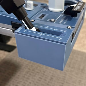 May include: Close-up of a blue control panel with a black lever and white markings. The panel has a gauge that reads "FULL" and "1/2". A black marker is positioned over the gauge.