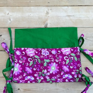 May include: A green and purple fabric pouch with floral print and green ties. The pouch has two pockets and is ideal for organising small items.