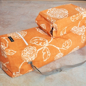 May include: Orange and white floral patterned yoga mat bag with a zipper and a matching smaller bag. The bag has a gray adjustable strap.