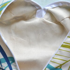 May include: A white fabric bag with a zipper closure. The bag has a green and blue geometric pattern on the outside and a white lining on the inside.