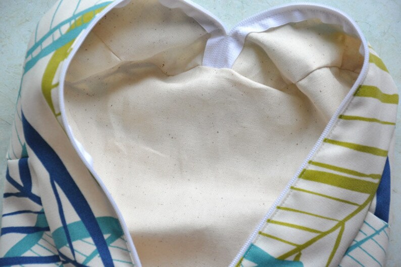 May include: A white fabric bag with a zipper closure. The bag has a green and blue geometric pattern on the outside and a white lining on the inside.
