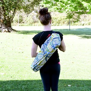 May include: A woman is carrying a yoga mat bag with a colorful abstract pattern. The bag is worn over the shoulder and has a strap.