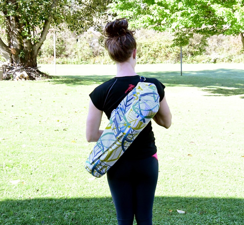 May include: A woman is carrying a yoga mat bag with a colorful abstract pattern. The bag is worn over the shoulder and has a strap.