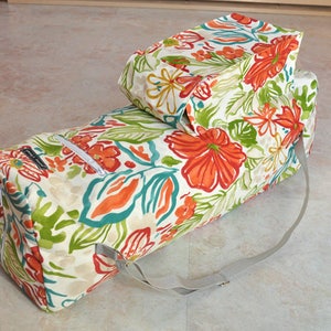 May include: A white yoga mat bag with a floral print in shades of orange, green, and blue. The bag has a zipper closure and a long strap.