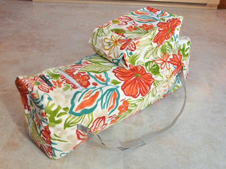 May include: A white yoga mat bag with a floral print in shades of orange, green, and blue. The bag has a zipper closure and a long strap.