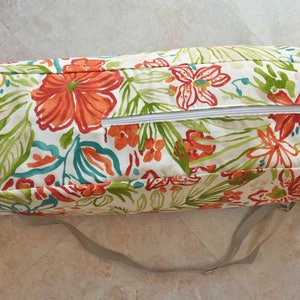 May include: A white, floral patterned zippered storage bag with a long, gray strap. The bag has a zipper closure and is made of a durable fabric.