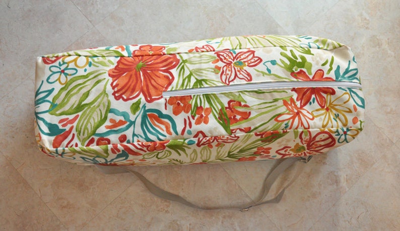 May include: A white, floral patterned zippered storage bag with a long, gray strap. The bag has a zipper closure and is made of a durable fabric.