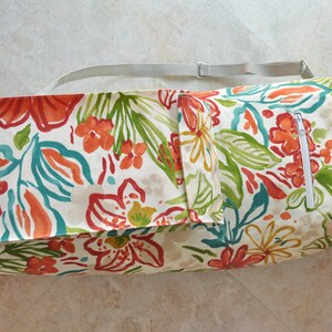 May include: A white canvas yoga mat bag with a floral print in shades of orange, red, green, and blue. The bag has a zippered pocket and a shoulder strap.