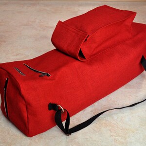 Pu&ograve; includere: Borsa da viaggio in tela rossa con una tracolla nera e una piccola borsa in tela rossa fissata in cima.