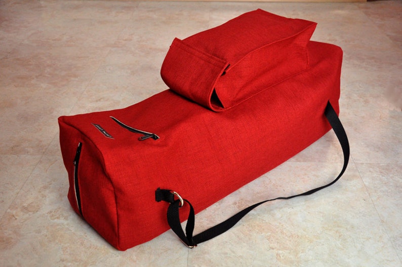 Pu&ograve; includere: Borsa da viaggio in tela rossa con una tracolla nera e una piccola borsa in tela rossa fissata in cima.