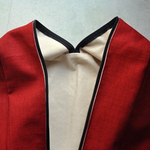 Pu&ograve; includere: Borsa in tessuto rosso con bordatura nera e fodera bianca. La borsa &egrave; piegata a met&agrave; e la fodera &egrave; visibile.
