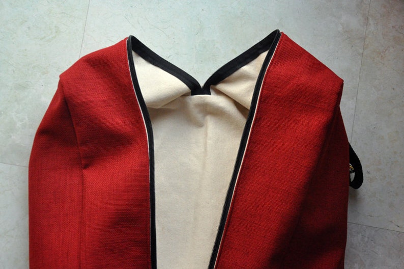 Pu&ograve; includere: Borsa in tessuto rosso con bordatura nera e fodera bianca. La borsa &egrave; piegata a met&agrave; e la fodera &egrave; visibile.